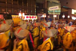 A group of dancers in yellow yukata and samurai style hats taking part in the competition