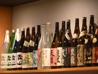Sake and shochu bottles line the wall shelf
