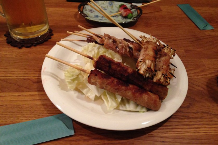 Selection of grilled skewers on a bed of fresh and crispy cabbage: tsukune (minced chicken) and enoki mushrooms wrapped in bacon