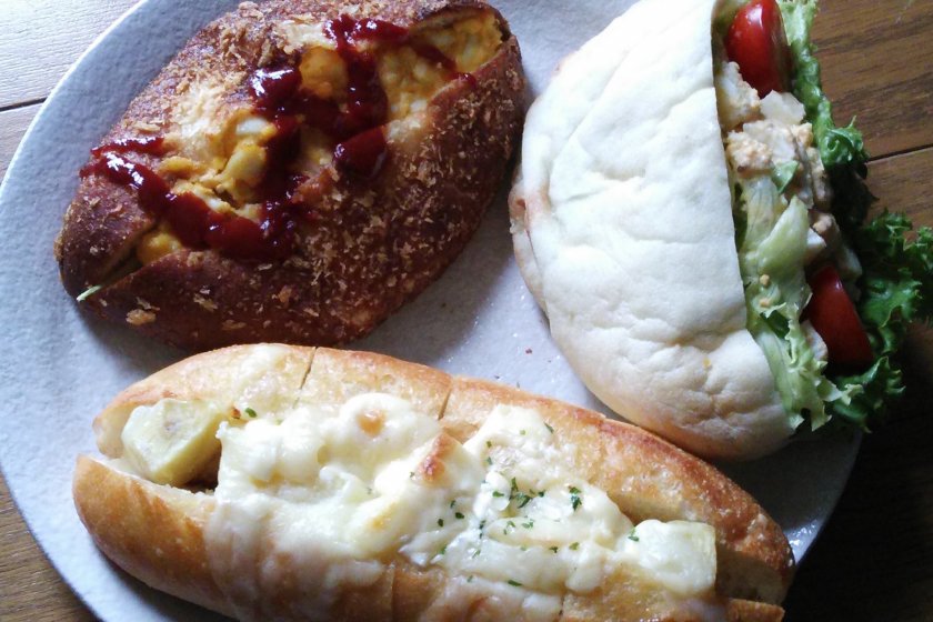 Top left is a special curry bread with egg and tomato sauce; to the right is a "pizza pita" with lettuce, tomato, egg and a creamy sesame dressing; and below is a bun filled with potato salad and covered in cheese.