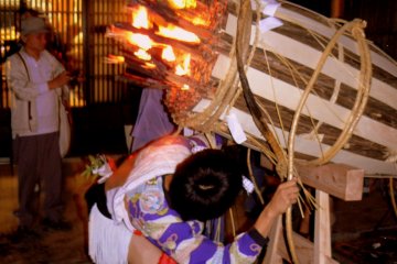 <p>A youth prepares to hoist one end of a giant torch onto his shoulder</p>