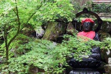 <p>Dark Buddha statue clad in red sits silently in front of the Kisshōkaku Hall</p>