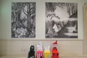 Stinky, Moominmamma, Hattifattener and Little My chairs lined up in front of enlarged works by Jansson for families to take pictures&nbsp;with their children&nbsp;