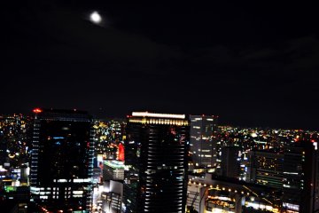 <p>ภาพพระจันทร์เต็มดวงกับแสงไฟจากตึกสูงยามค่ำคืน</p>