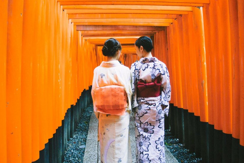 Dua orang gadis Jepang yang berpakaian tradisional; kimono dan yukata, sedang berjalan di antara rubuan torii.
