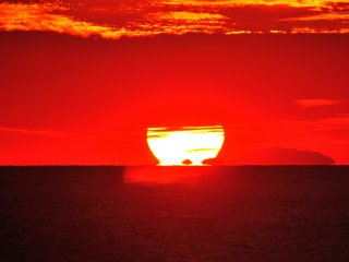 太陽が水平線に沈む直前の現象ダルマの形に似る事から我々は&rdquo;ダルマ夕日&rdquo;と呼んでいる　今回は惜しくも上部が雲に隠れ不完全な形に終わった