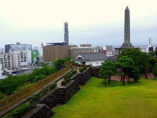 A tall monument stands in the park near the reconstructed Yamanote Gomon gate