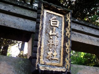 Golden signage of Hakusan Shrine hanging on the stone torii gate
