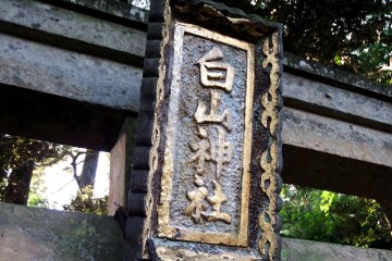<p>Golden signage of Hakusan Shrine hanging on the stone torii gate</p>