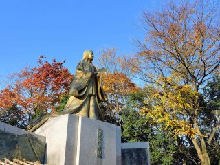 秋の紅葉と青空の下、黄金色に輝く紫式部の銅像