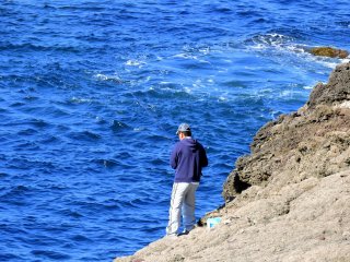 切り立つ岩から釣りをする男性