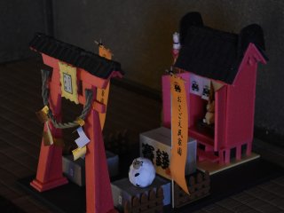 床の間に飾られたミニチュアの神社と鳥居。オレンジ色の旗には「おさごえ民家園」と書かれている。