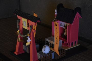 <p>Miniature shrine and torii gate displayed inside a house. The orange banner says &#39;Osagoe Folk Museum Village&#39;.</p>
