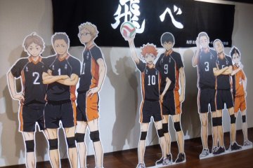 <p>The cafe is filled with things related to the anime. Here are the characters by a banner with their motto on it.</p>