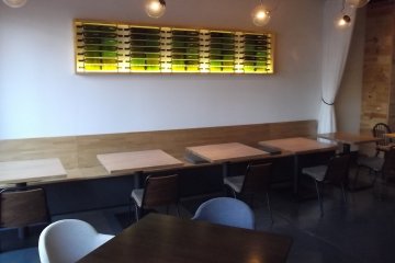 <p>Wine bottles decorate the wall above the tables</p>