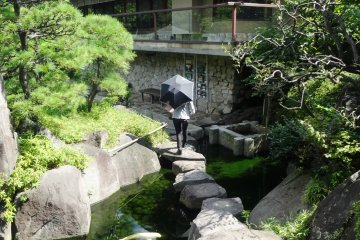 <p>A woman crosses a path of stepping stones in front of the teahouse</p>