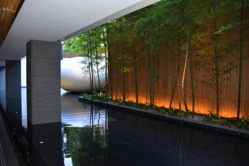 Open-air corridor of the hotel. Bamboo and a moon-shaped sculpture are set in an artificial pond.