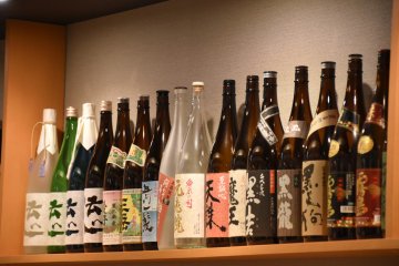 <p>Sake and shochu bottles line the wall shelf</p>
