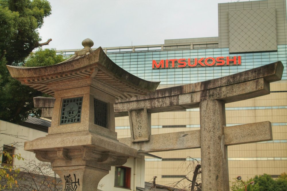 โคมไฟหินและประตูของศาลเจ้าเกะโกะกับห้างสรรพสินค้า Mitsukoshi ในพื้นหลัง