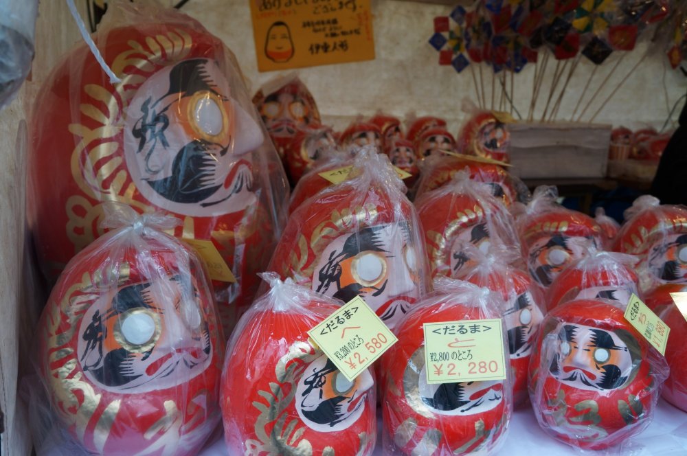 Daruma of various sizes wrapped in plastic to protect them from the rain.
