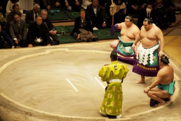 The Yokozuna (top ranker wrestler) champion makes a ceremonious entrance into the ring, flanked by two makuuchi wrestlers