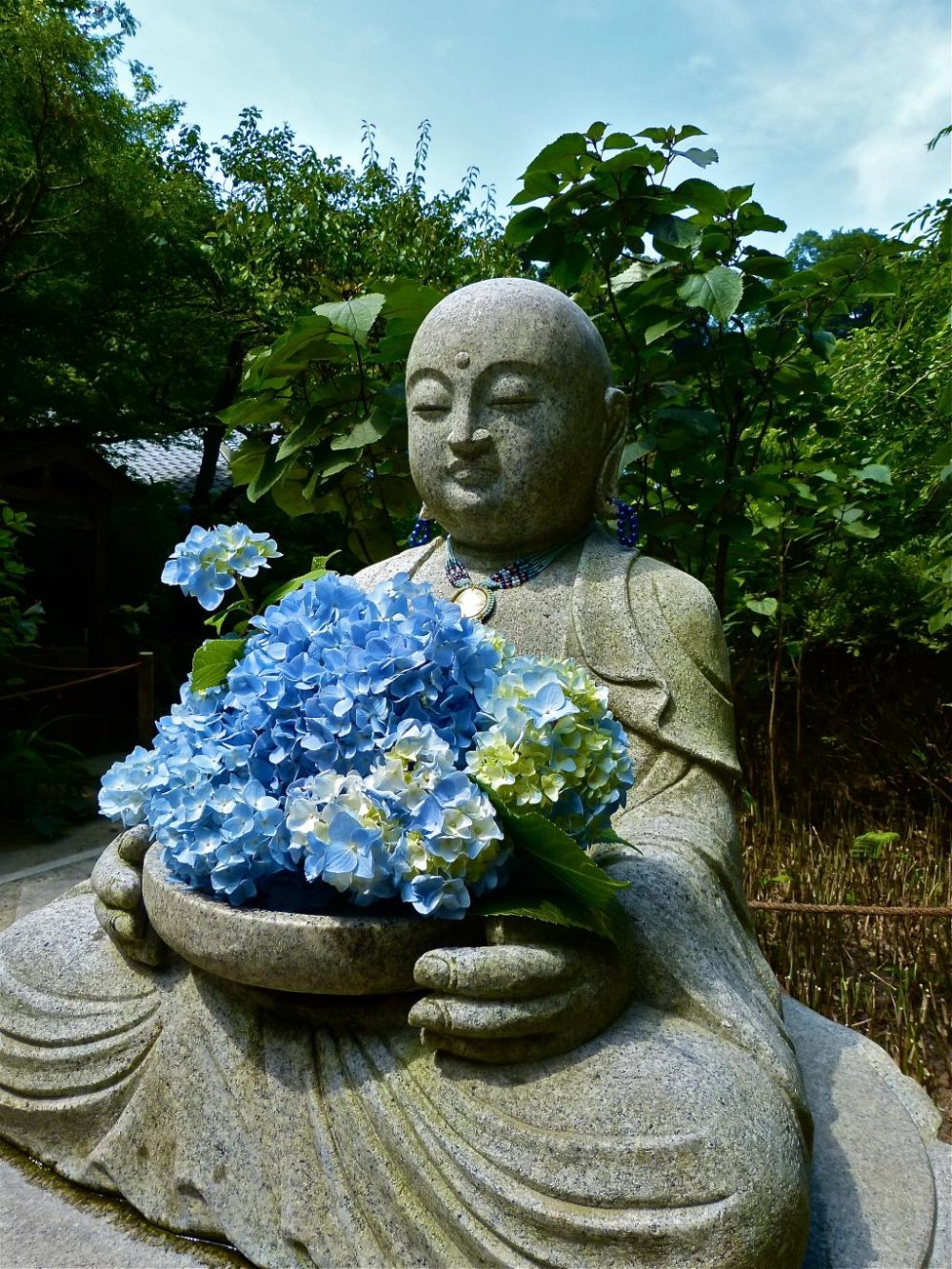 Une statue de jizo tenant des hortensias bleus