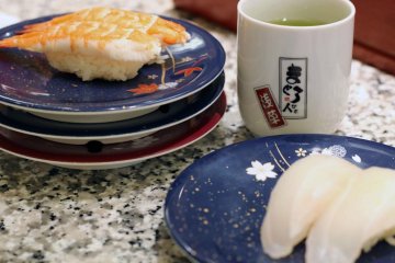 The pile of plates is growing. Here we see ebi (shrimp) and madai (red snapper). Enjoy complementary green tea with your meal.