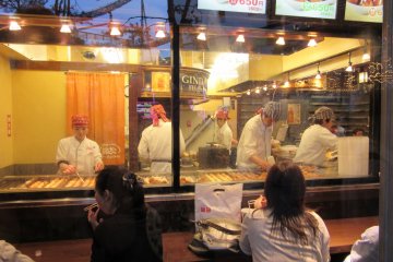 Chefs cooking takoyaki behind glass window