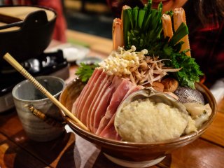 Vợ của Okawa-san Saiko hỗ trợ trong việc cho càng cua, tôm, gà, đậu phụ, nấm shiitake, sò điệp và rau xanh vào súp sôi
