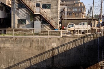 Shakujigawa near Yamate-dori: The shadow of a bridge seems as a staircase down to the riverbed. By chance it is in the opposite direction to the building's stairway, which in turn casts shadows on the side of the building. These are bisected by the roadsi