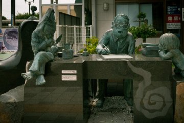 <p>รูปปั้นหินกับทองแดงขนาดเท่าตัวจริง ของอาจารย์มิซุกิขณะทำงาน โดยมีตัวละครในเรื่องนั่งอยู่ข้างๆ</p>