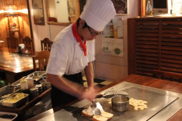 <p>Dinner ingredients come out on a cart; here a chef is preparing potatoes and french bread</p>