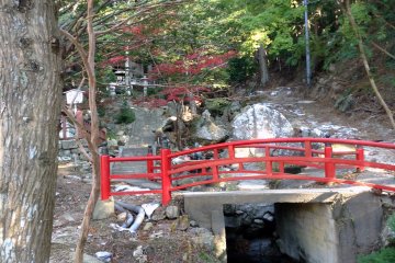 A vermillion bridge spans a small stream behind the main shrine.